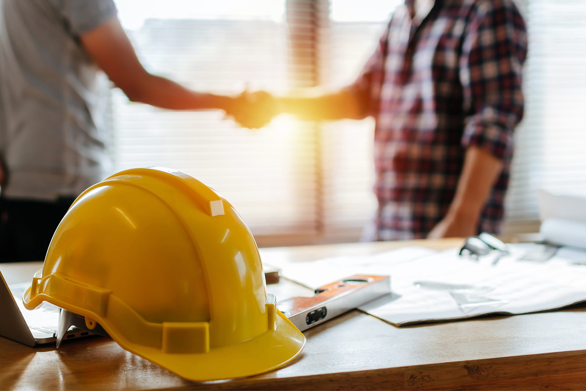 Safety helmet on desk with workers shaking hands